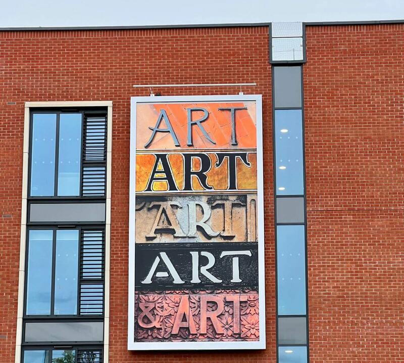Image showing the artwork attached to the side of a four storey red-brick building. The artwork is the word 'art' in stylised typeface letters 