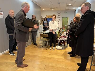 A group of nine people meeting in an art gallery space, talking to MP Ellie Chowns about the Our Place programme.