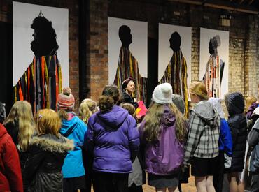 Megan Clark-Bagnall and pupils visit Faye Claridge's Inventive Offspring an art exhibition with 5 large artworks on a brick wall.