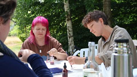 Image of three people taking part in creative activity in the outdoors. One has bright pink hair.