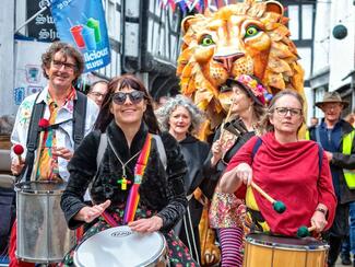 A giant lion puppet in Leominster with a crowd made up of Broseley Beats Samba Band