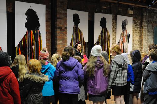 Megan Clark-Bagnall and pupils visit Faye Claridge's Inventive Offspring an art exhibition with 5 large artworks on a brick wall.