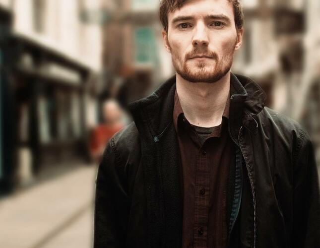 Image of singer George Boomsma, a white man with short brown hair and stubble, facing the camera.