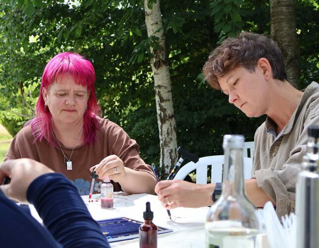 Image of three people taking part in creative activity in the outdoors. One has bright pink hair.
